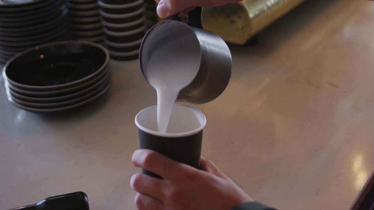 Hands of mixed race male barista wearing an apron preparing takeaway coffee