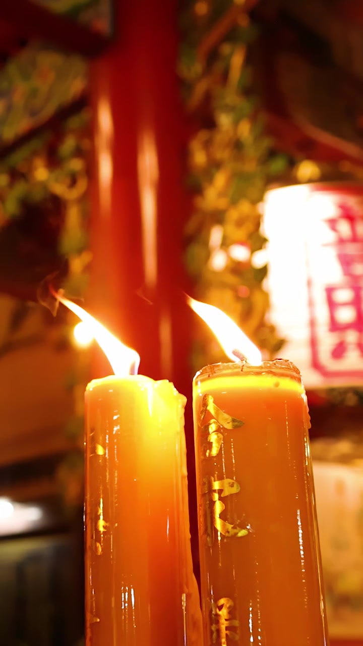 Due grandi candele bruciano con fiamme tremolanti in un tempio ornato, con calda illuminazione ambientale da lanterna
