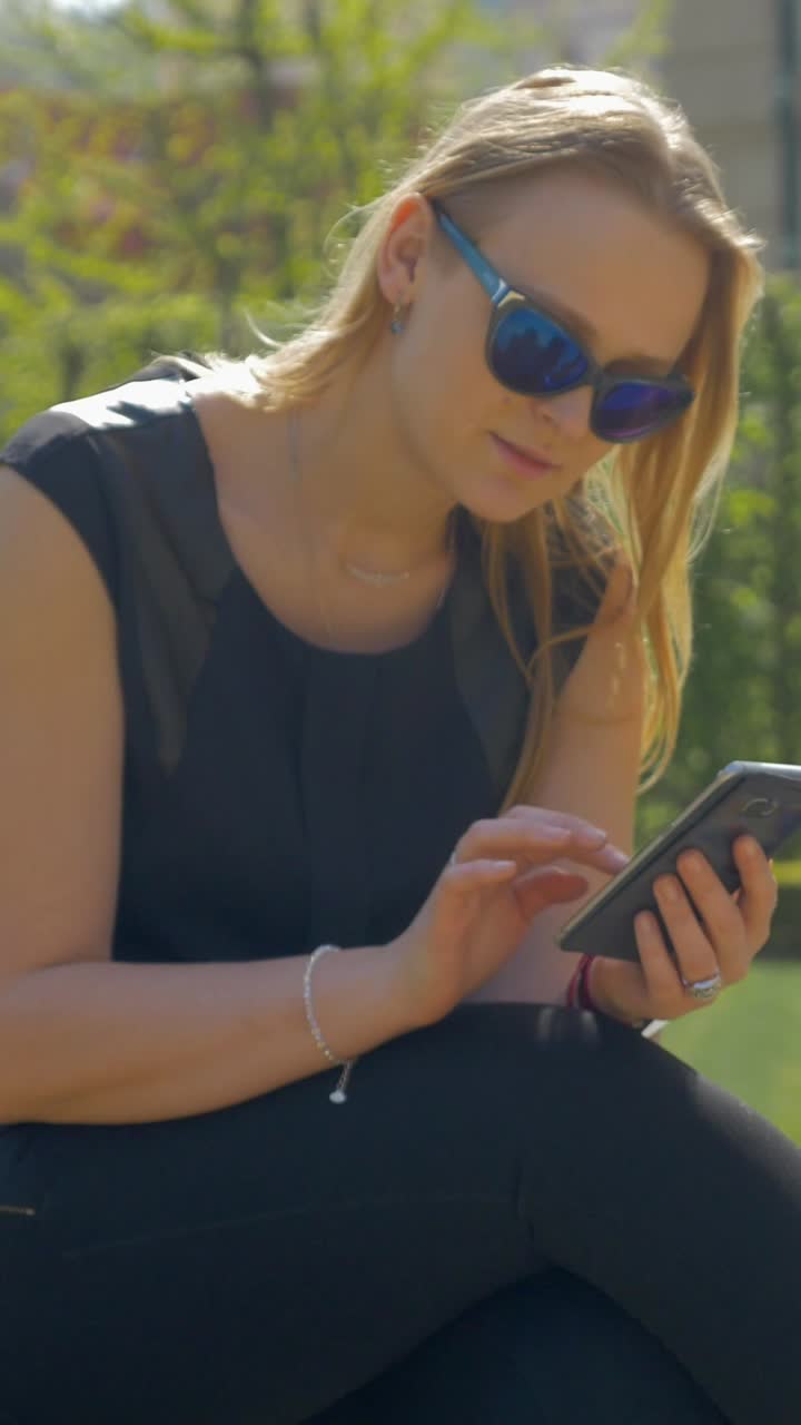 Giovane donna con occhiali da sole che usa lo smartphone all'aperto in un parco