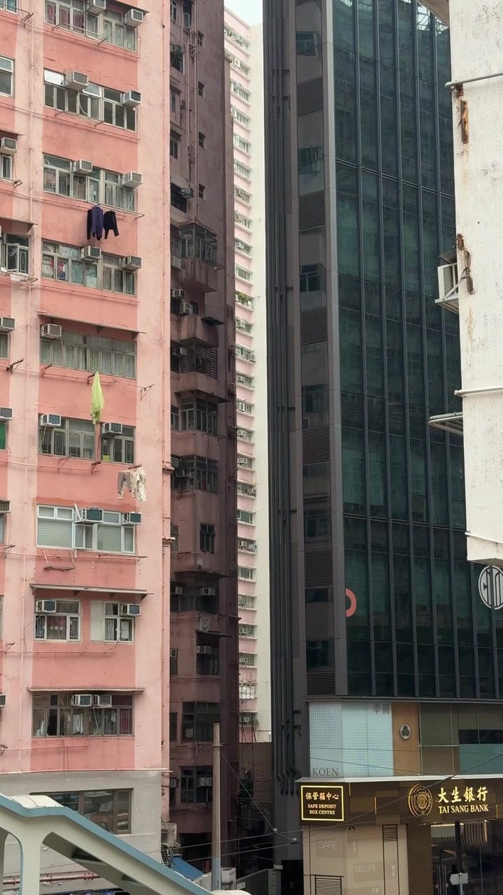 Plano médio vertical de edifício residencial rosa adjacente a edifício comercial de vidro e ao Banco Tai Sang em Hong Kong
