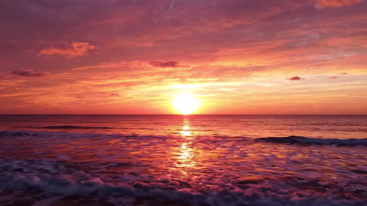 A breathtaking sunset paints the sky in vibrant hues of orange, pink, and purple, casting a warm glow over the tranquil ocean waves, creating a serene and picturesque scene.