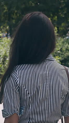 slow motion backside close view young slim woman in striped dress walks in pictorial green park on summer day