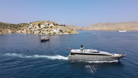 Lujoso-Yate-Gris-Saliendo-Del-Puerto-De-Symi-En-Grecia,-Hermoso-Día-De-Verano,-Aéreo