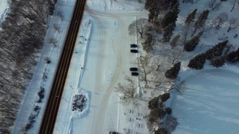 Aéreo-Invierno-Sobrevuelo-Paralelo-Cubierto-De-Nieve-Vista-De-Pájaro-Puesta-De-Sol-Volar-Sobre-El-Norte-De-Saskatchewan-Río-Estacionamiento-Vacío-Siguiente-Pista-De-Patinaje-Sobre-Hielo-Artificial-Más-Grande-En-Canadá-En-El-Pabellón-Victoria-Park-Pavillion-Ice1-3