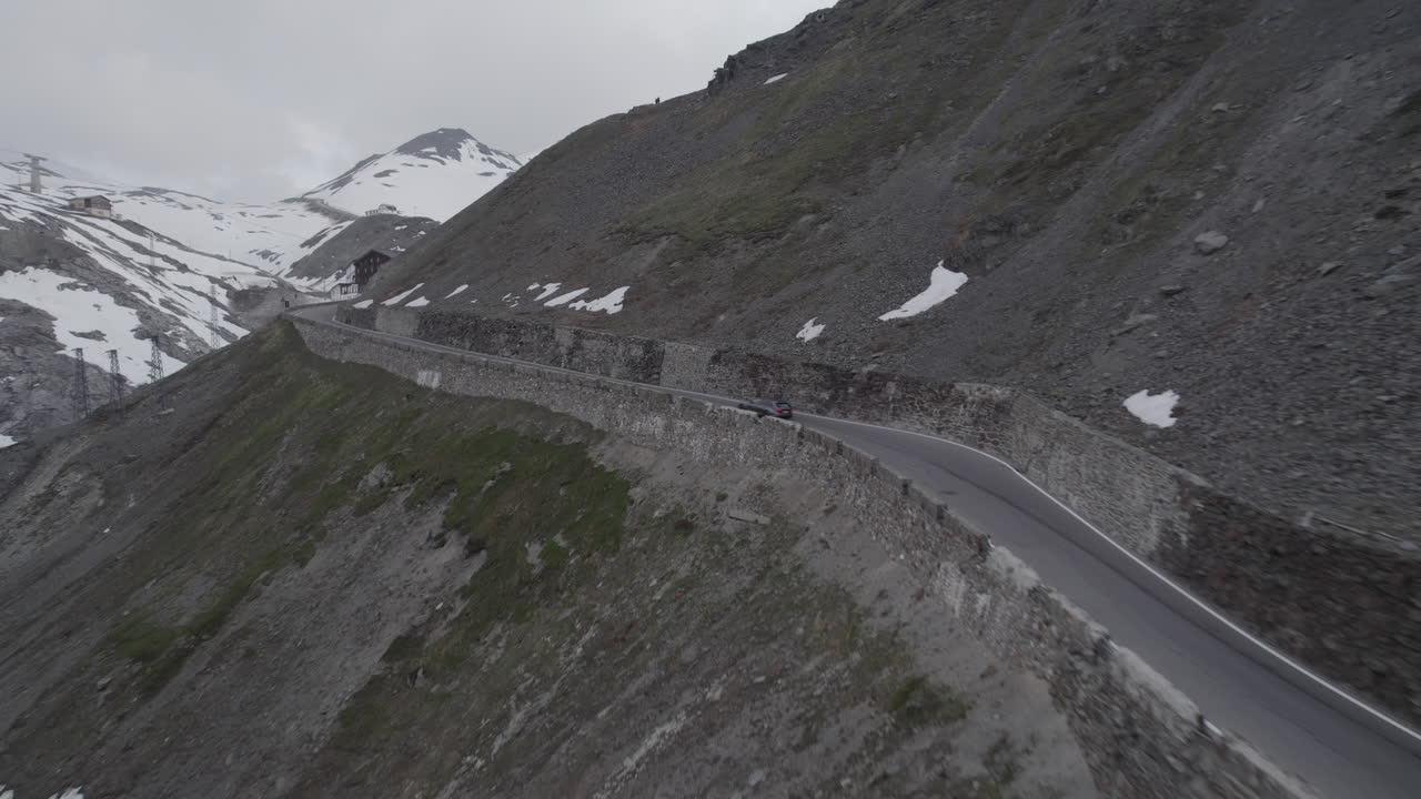 스텔비오 패스 (stelvio pass) 에서 언덕을 올라가는 차의 드론  (drone shot) 이탈리아의 회색 날, 눈이 쌓인 산에서 휘어지는 도로 로그