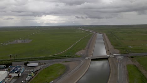 Empuje-Lento-De-Drones-Sobre-Un-Sereno-Canal-Californiano-Después-De-La-Lluvia-Y-Grandes-Campos-Verdes