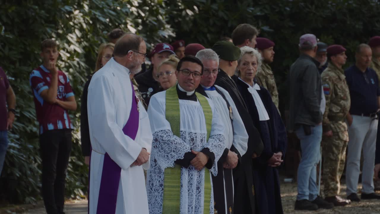 Group of clergymen, dressed in ceremonial robes, engage in conversation during commemorative event at Oosterbeek War Cemetery. Soldiers and onlookers are present in background. Oosterbeek, Gelderland