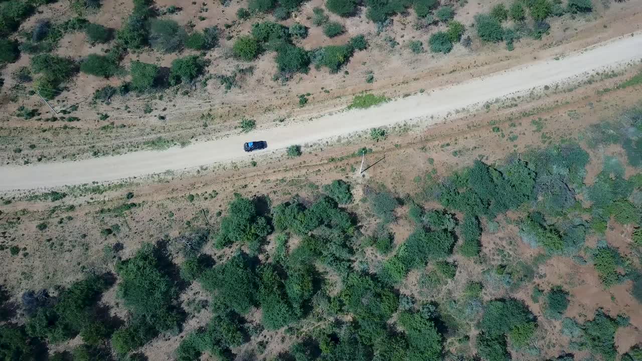toma aérea de seguimiento de un jeep conduciendo por un camino de tierra sobre un páramo remoto en áfrica.