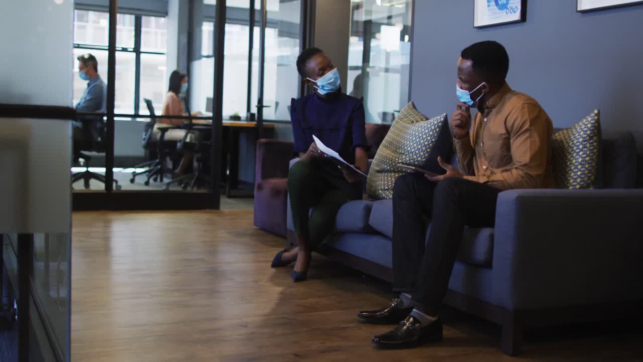Diverse male and female office colleague wearing face masks discussing at modern office