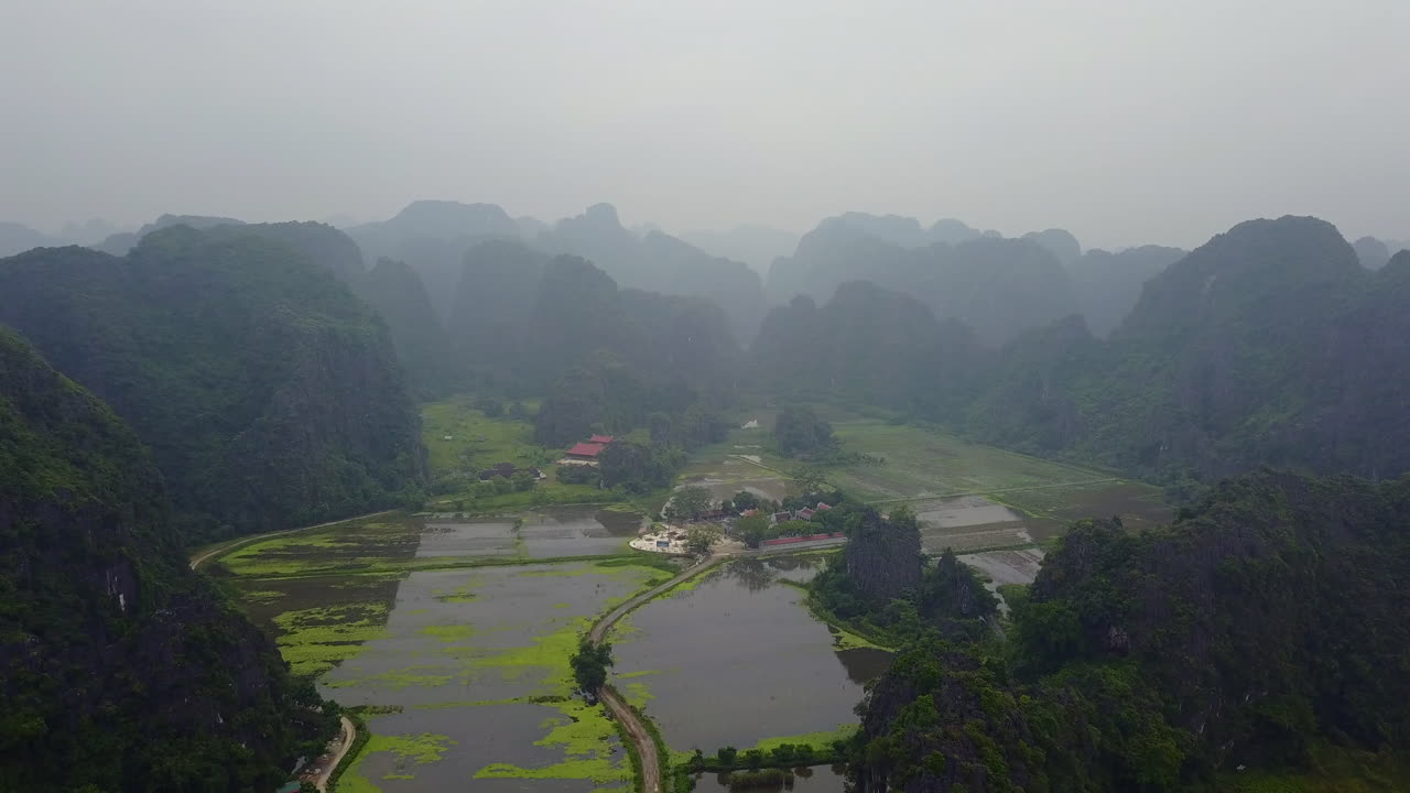 Experience the serene beauty of a cloudy and rainy day in Ninh Binh, Vietnam, as the mist settles over the lush rice plantations nestled amidst the majestic limestone karsts