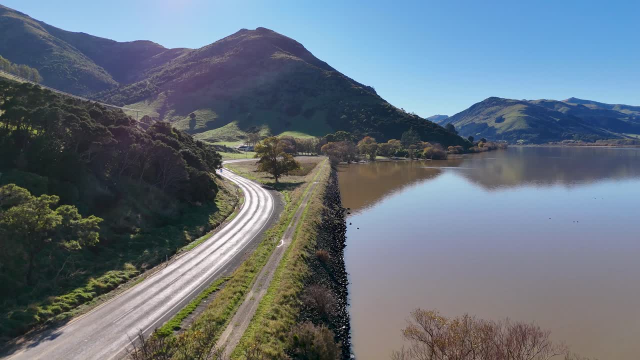 Aerial view of Akaroa's winding roads and tranquil lake, captured in bright daylight with lush green hills