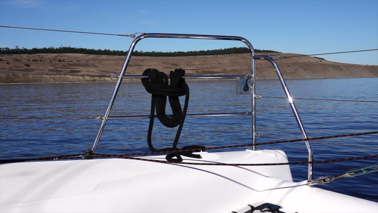 Camera looking at the port railing of a catamaran sailing with the San Juan Islands in the background on a sunny and clear day