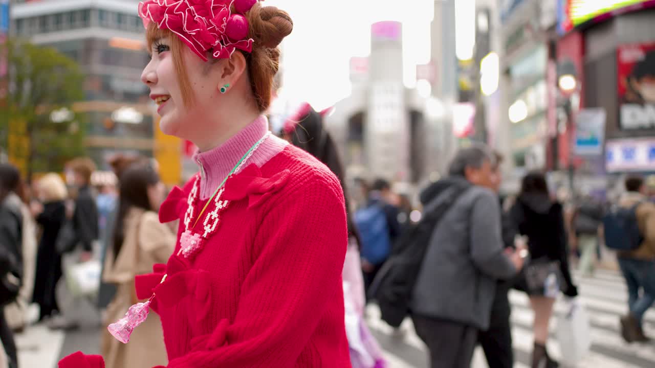 Chicas japonesas con atuendos de color rosa brillante caminan y hablan entre la multitud en una intersección concurrida.