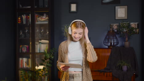 happy young woman with headphones listening music on tablet and dancing in living room at home