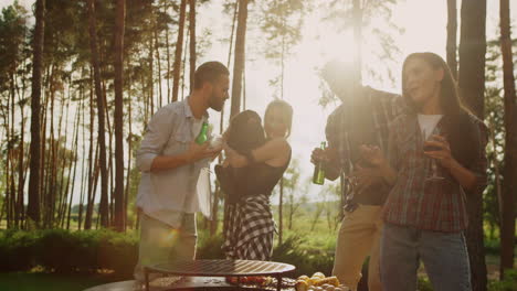 cheerful friends dancing on bbq party in forest. woman holding dog outdoors