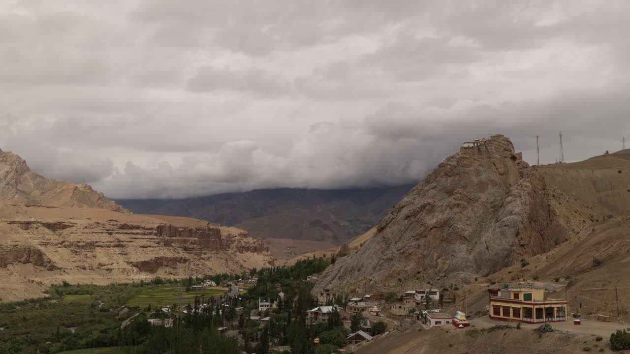 Ominous storm clouds swirl around peaks in Mulbekh a mountainous landscape, with clif top monastery