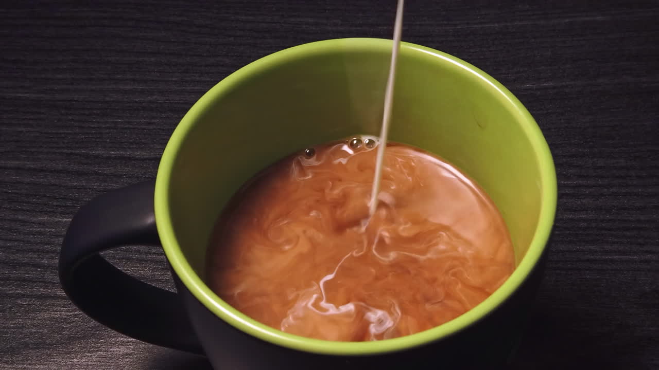 Rallentatore ravvicinato di un uomo caucasico che versa latte in una tazza di ceramica con caffè nero su un tavolo di legno
