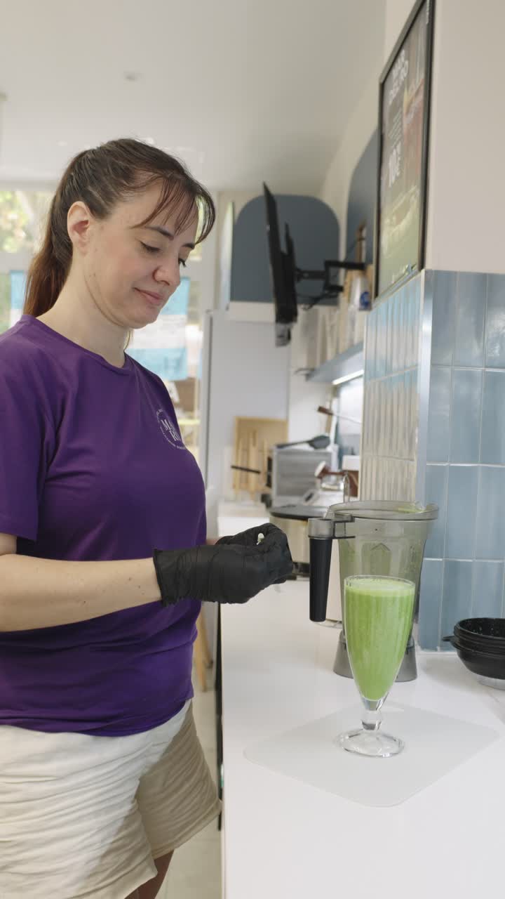 Woman preparing a green smoothie with a blender in a kitchen