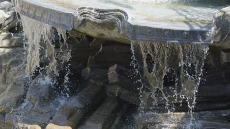 clear water cascades over sculpted stone fountain, splashing onto rocks in bright natural daylight