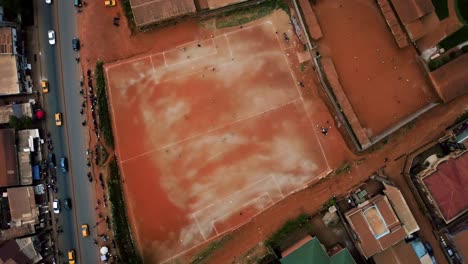 people playing street football on a red clay field in the city of africa - rotating, high angle, drone shot