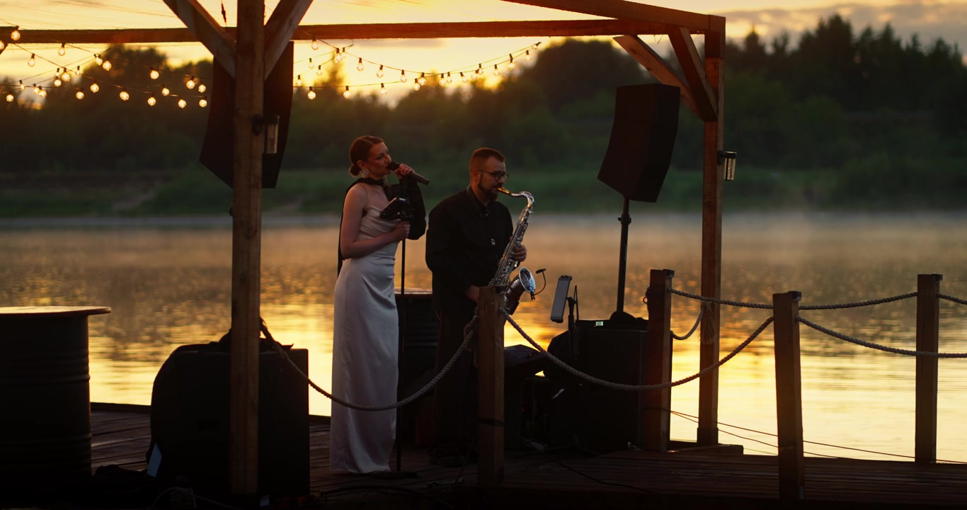 Duo musicale che si esibisce su un molo di legno al tramonto
