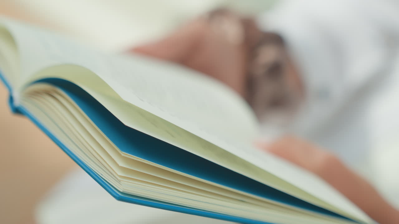 Primo piano di mani che tengono un diario aperto, scrittore caucasico in una luce interna soffusa che sfoglia lentamente le pagine, carta testurizzata e copertina blu a fuoco, atmosfera accogliente e tranquilla per studio e revisione di appunti.