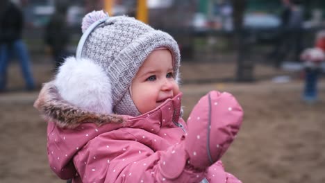 young happy caucasian toddler girl in warm clothes having fun on public playground carousel on cold autumn winter day