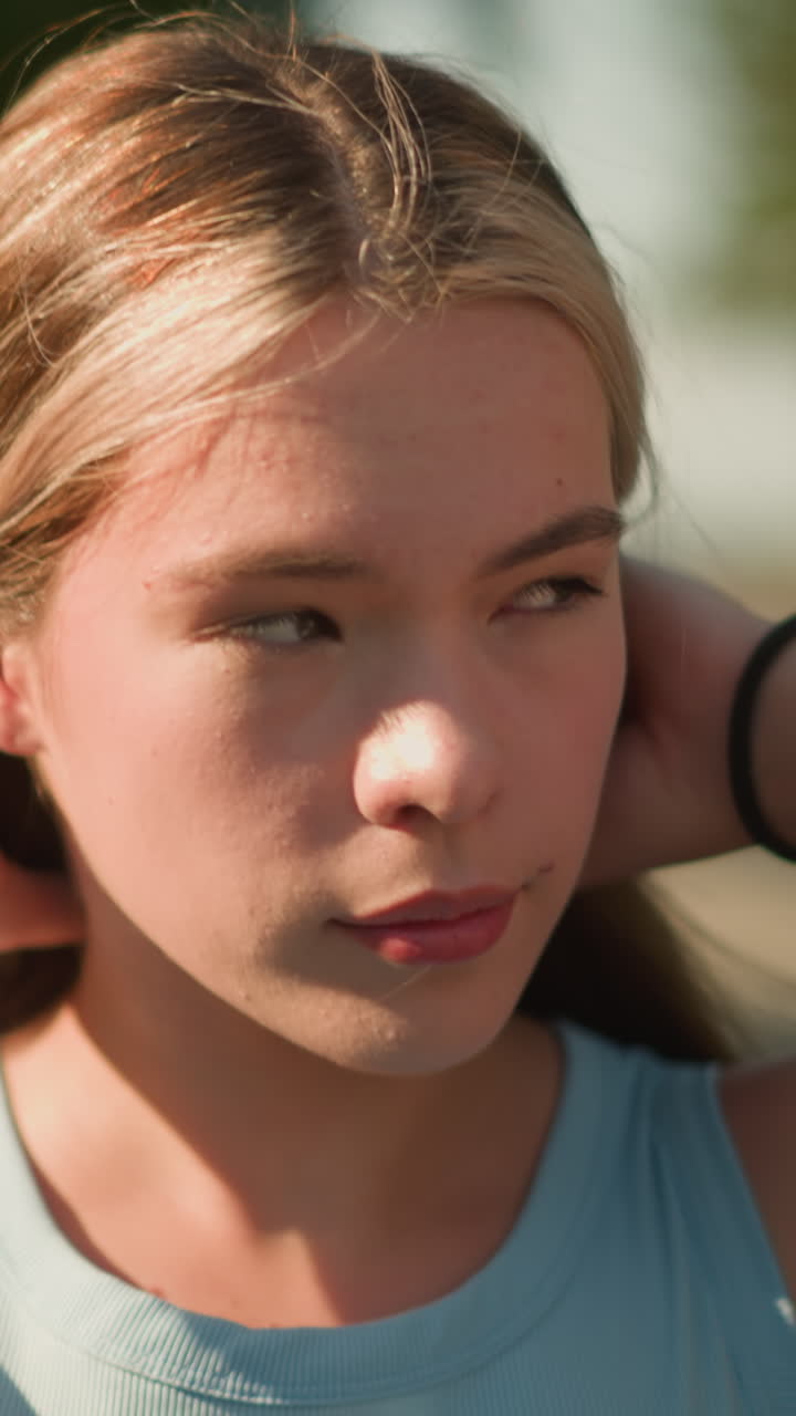 Close-up of lady parking her hair to the back while glancing into distance, with sunlight reflecting on her hands, wearing a black hand bangle, softly blurred background featuring greenery
