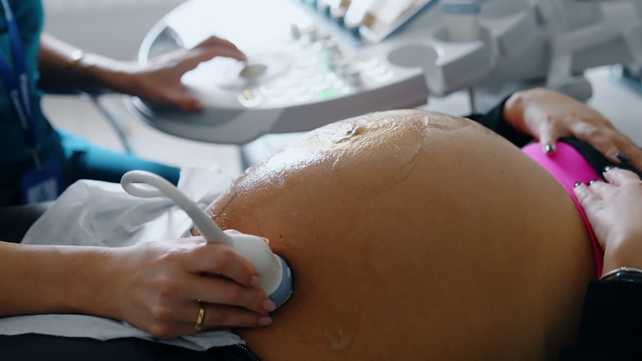 Big belly of a pregnant woman with gel on it. Hand of doctor moves ultrasound device by the patient's abdomen. Close up.