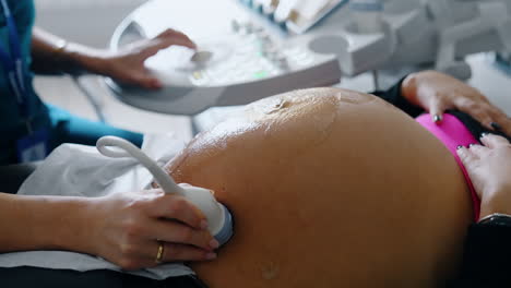 big belly of a pregnant woman with gel on it. hand of doctor moves ultrasound device by the patient's abdomen. close up.