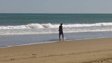 Hombre-Alto-Camina-En-Olas-Poco-Profundas-En-La-Orilla-Arenosa-En-Verano,-Cámara-Lenta