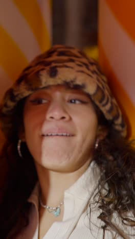 a woman in a leopard print bucket hat with various expressions against an orange and white striped background