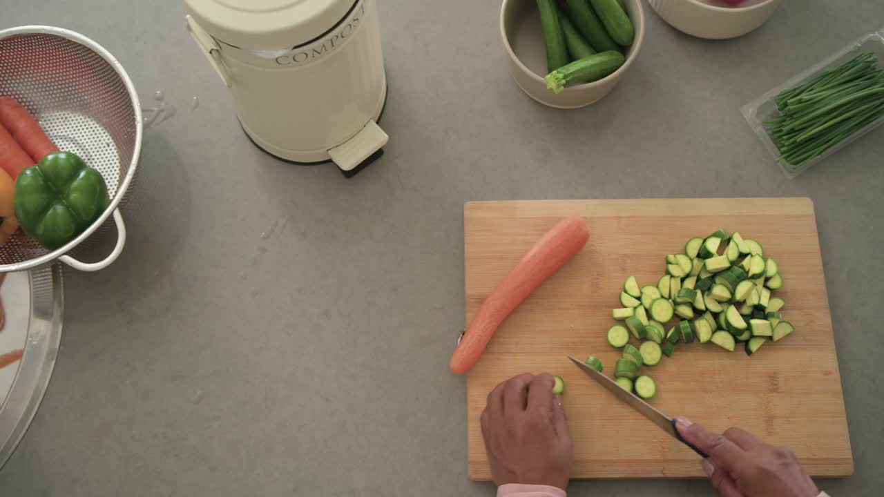 La telecamera si avvia, mani sinistre pelano carote mentre mani destre affettano zucchine per la preparazione del pasto.