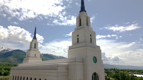 Smooth-drone-shot-of-the-Layton-LDS-Mormon-Temple-moving-from-side-to-the-right-and-up-seeing-blue-sky-and-Wasatch-mountains-in-back-ground