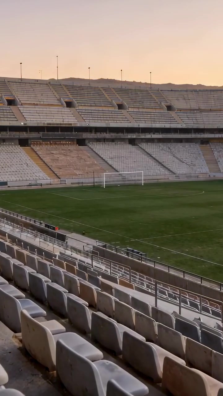 Vertikales Video: Sonne sinkt, funkelnde Lichter, leerer Fußballplatz und leuchtende Tribünen im Stadion