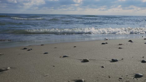 Stones-In-The-Sand-With-Waves-Breaking-On-The-Beach-During-Sunset