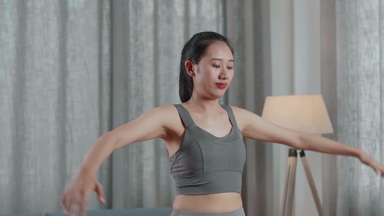젊은 아시아인 트레이너 여성 스포츠 옷을 입고 집에서 운동을 가르치면서 말하고 스트레칭하고 있습니다.