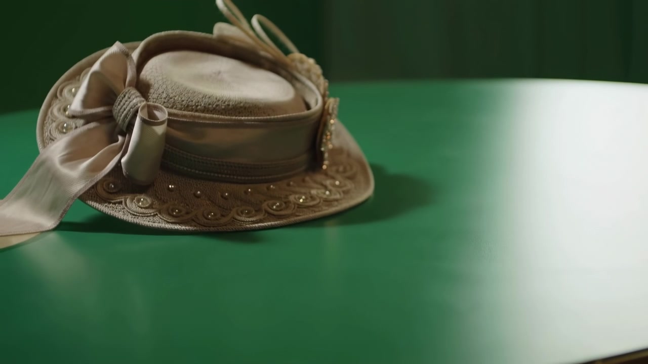 Cappello beige su tavolo verde, accessorio vintage di paglia con nastro e finiture di perline, illuminazione morbida da studio, profondità di campo ridotta.