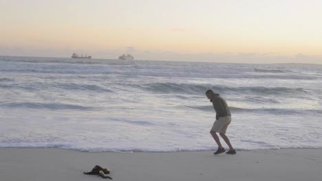 man walking on beach and avoids ocean wave water as he laughs