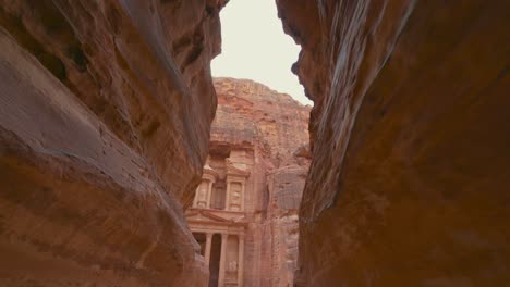 walking toward the treasury through the siq at petra, historic unesco heritage site carved into sandstone in jordan. famous indiana jones last crusade filming location and tourist destination khaznet. revealing shot.