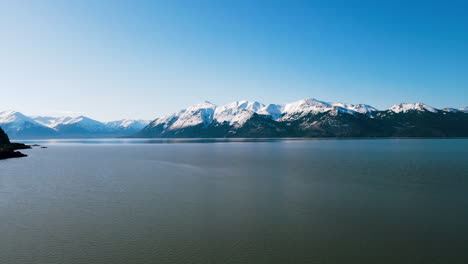 aerial: mountains in alaska next to lake with blue sky and snowy peaks