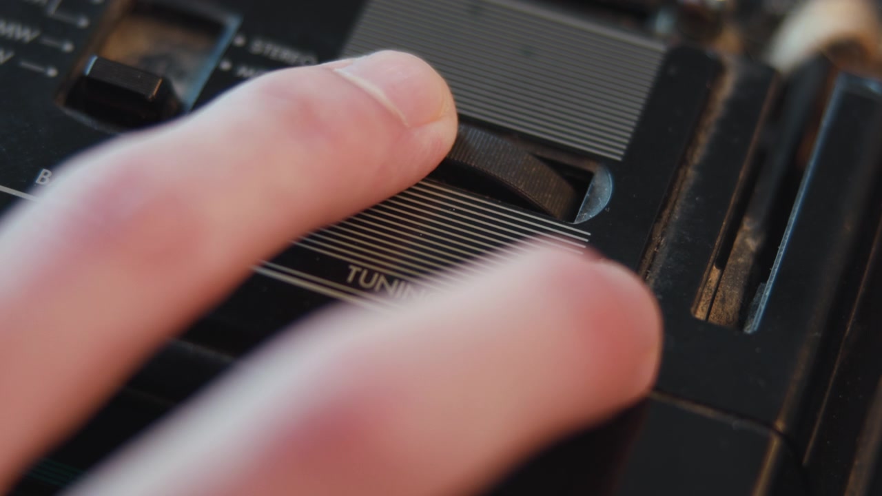 Hvid hånd justerer vintage radioknap, nærfokus på riflet urskive og tekstureret overflade, retro lyd