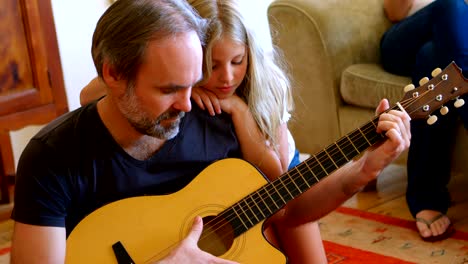 father playing guitar with her daughter in living room 4k