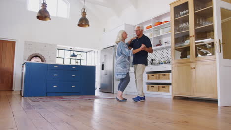 una pareja de mayores en casa bailando juntos en la cocina.