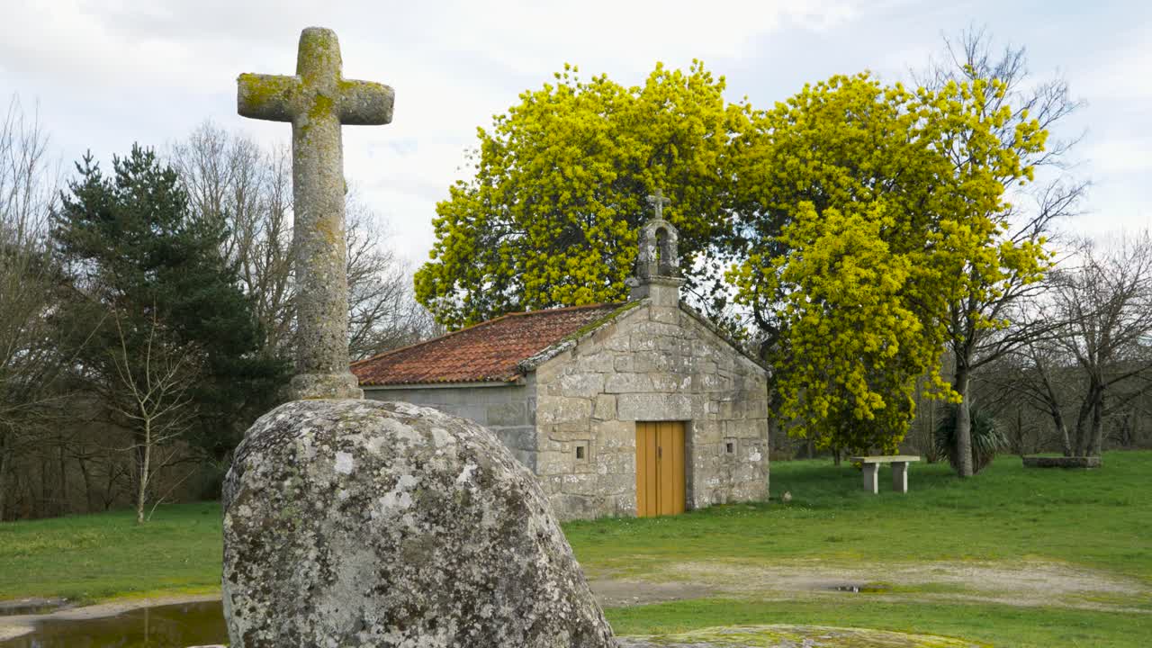 Static view of moss covered stone carved round cross in front of Chapel of San Vitoiro with yellow tree