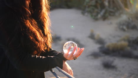 close up on the hands of a beautiful woman wearing a ring and holding a magic crystal ball in the bright sunlight during golden hour sunset