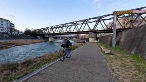 cyclist on a path next to a river and bridge