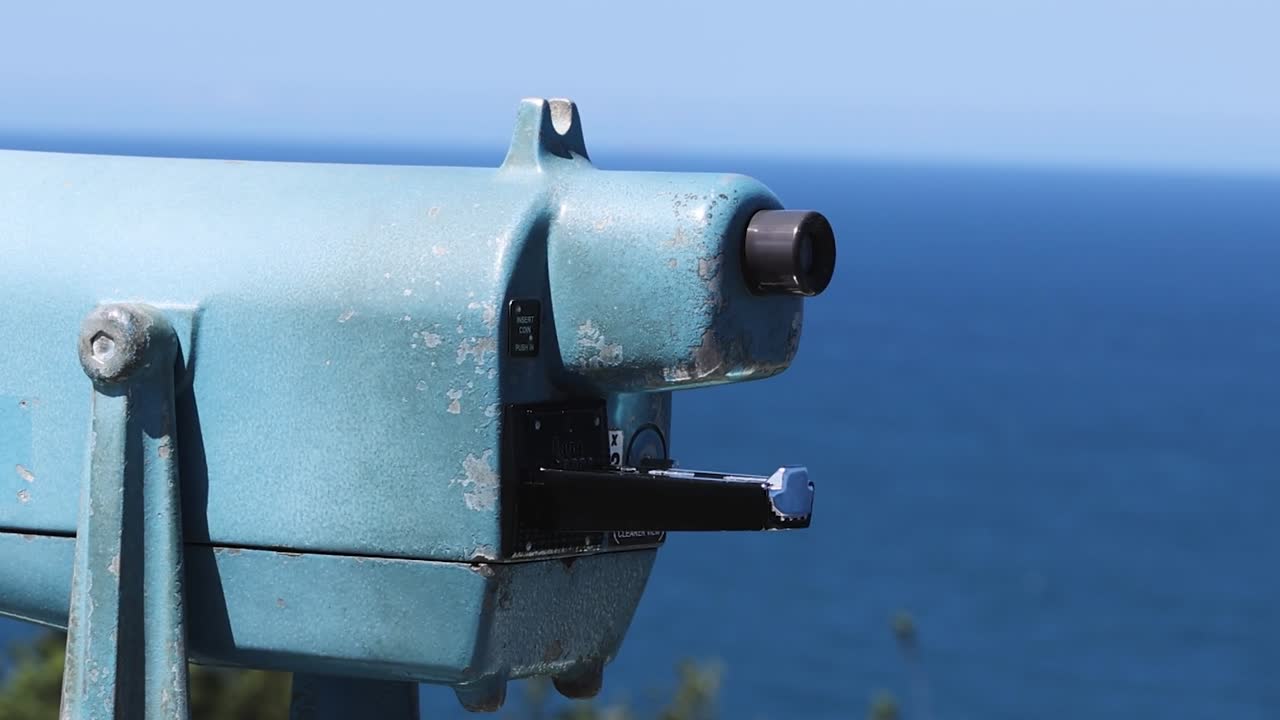 Detailed view of stationary binoculars facing the ocean, highlighting their structure and design against a blue seascape.