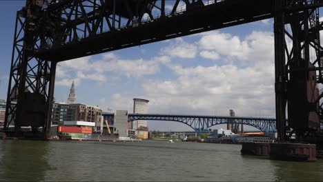 Cleveland,-Ohio,-Time-lapse-Del-Río-Cuyahoga-Con-Un-Puente-De-Tren-En-Primer-Plano-Mientras-Las-Nubes-Pasan-Por-Whiskey-Island-En-Wendy-Park-En-La-Costa-Del-Lago-Erie