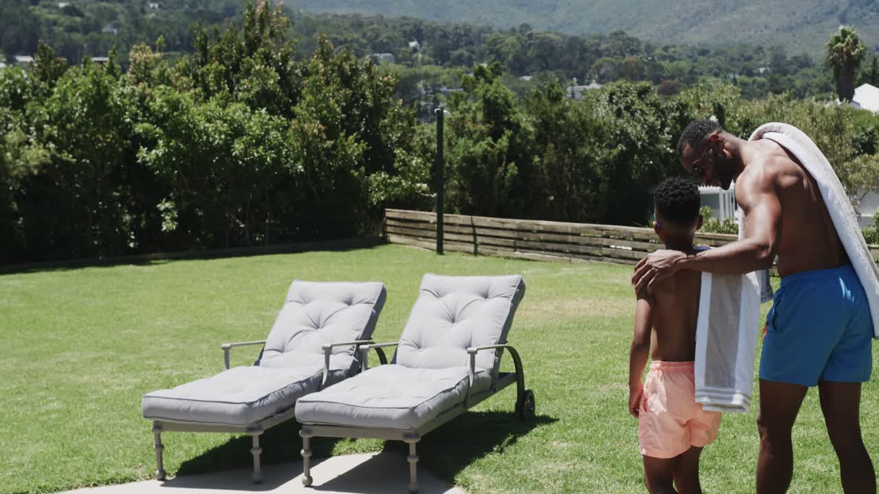 African American father guiding son to pool edge, placing hand on shoulder with towel, copy space
